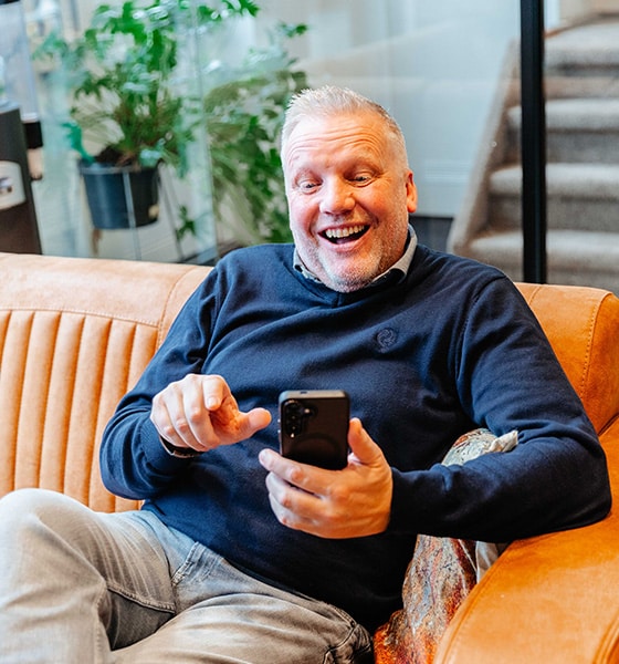 Makelaar kijkt enthousiast naar zijn telefoon