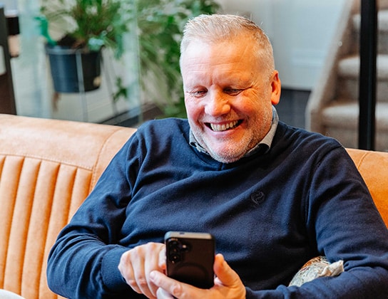 Makelaar kijkt lachend naar zijn telefoon